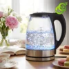 Bouilloire electrique verre lumineuse avec eau bouillante et bulles, posée sur table près de macarons et fleurs roses