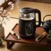Bouilloire thermostat ecran tactile noire en verre et métal affichant 100 degrés sur un plateau en bois avec du thé noir