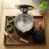 Vue plongeante d'une bouilloire thermostat ecran tactile ouverte avec accessoires de thé japonais sur plateau en bois