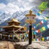 Close-up of a brass moulin priere tibetain mantras with a dark wooden handle against a scenic mountain temple backdrop