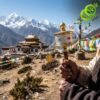 Close-up of a hand holding a golden moulin priere tibetain mantras against a backdrop of snowy peaks and a monastery