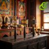 Three brass moulin priere tibetain mantras with different metal finishes resting on a dark rustic wooden altar table