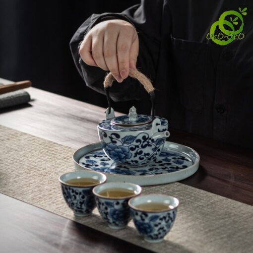 main versant du thé d'un service porcelaine bleu et blanc motif lotus sur une table en bois avec trois tasses remplies