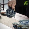 Service thé porcelaine bleu et blanc motif lotus traditionnel, main verse thé dans tasse, détails décoratifs en bleu sur céramique fine