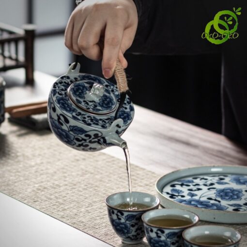 Service thé porcelaine bleu et blanc motif lotus traditionnel, main verse thé dans tasse, détails décoratifs en bleu sur céramique fine