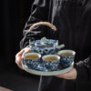 Service thé porcelaine bleu et blanc motif lotus traditionnel tenu par une main, détails des tasses et théière avec poignée en corde naturelle