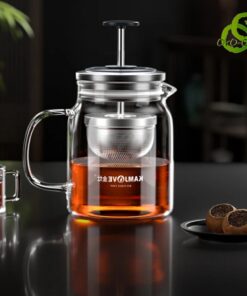théière en verre transparent avec filtre métallique descendable et remontable, remplie d'une infusion ambrée, sur une surface noire réfléchissante