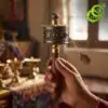 Molinillo de oración tibetano con mantras grabados | OkO-OKO™ Mano sosteniendo un molinillo de oraciones tibetano de latón y madera con mantras y símbolos grabados y un pequeño colgante de cadena metálica
