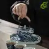 Blue and white porcelain tea set with a traditional lotus pattern | OkO-OKO™ a hand holding a blue-and-white porcelain teapot with a lotus pattern on a tray, along with three filled cups
