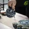 Blue and white porcelain tea set with a traditional lotus pattern | OkO-OKO™ Blue-and-white porcelain tea set with a traditional lotus pattern, featuring a figure pouring tea into a cup, with decorative blue details on fine ceramic