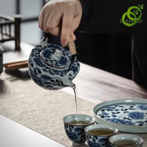 Blue and white porcelain tea set with a traditional lotus pattern | OkO-OKO™ Blue-and-white porcelain tea set with a traditional lotus pattern, featuring a figure pouring tea into a cup, with decorative blue details on fine ceramic
