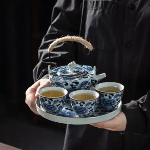 Blue and white porcelain tea set with a traditional lotus pattern | OkO-OKO™ Blue-and-white porcelain tea set featuring a traditional lotus design held by a hand, with details of the cups and teapot featuring a natural cord handle