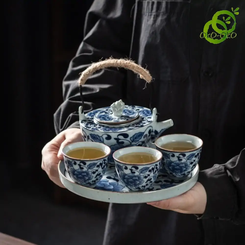 Blue and white porcelain tea set with a traditional lotus pattern | OkO-OKO™ Blue-and-white porcelain tea set featuring a traditional lotus design held by a hand, with details of the cups and teapot featuring a natural cord handle