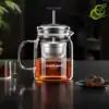 théière en verre transparent avec filtre métallique descendable et remontable, remplie d'une infusion ambrée, sur une surface noire réfléchissante
