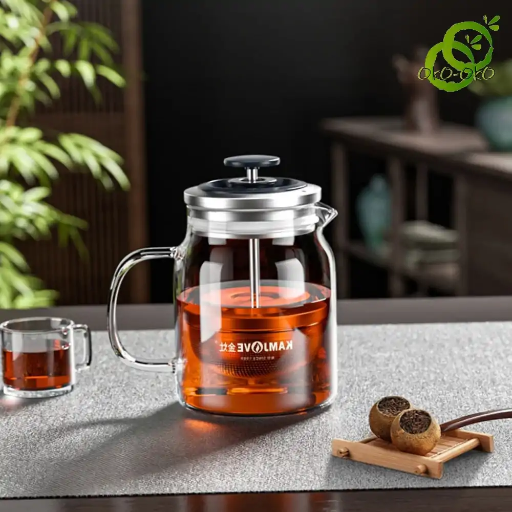 transparent glass teapot with integrated retractable filter, filled with dark red infusion, placed on a table with a cup and tea ball infusers transparent glass teapot with integrated retractable filter, filled with dark red infusion, placed on a table with a cup and tea ball infusers